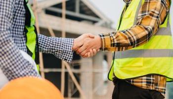 两名身穿安全背心的男子在商业建筑工地握手.
